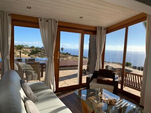 Ett rymligt rum med ett stort glasbord, bekväma sittplatser och utsikt över havet.