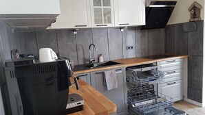 Eine moderne Küche mit weißen Schränken, einer schwarzen Dunstabzugshaube, einer Holz Arbeitsplatte und einem integrierten Geschirrspüler.