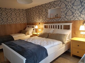 A bedroom with two beds, a bedside table with a lamp, a nightstand, and a wall-mounted shelf. - Apartment Rose by Interhome (Fritzlar)