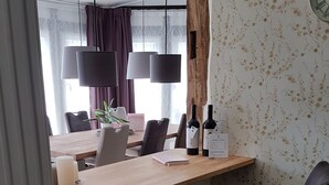 Ein Essbereich mit einem Holztisch, schwarzen Stühlen und hängenden Pendelleuchten. Auf dem Tisch stehen zwei Weinflaschen und ein Menüschild.