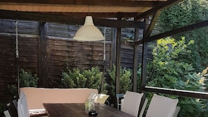 Eine überdachte Terrasse mit einem Holztisch und weißen, gepolsterten Stühlen.