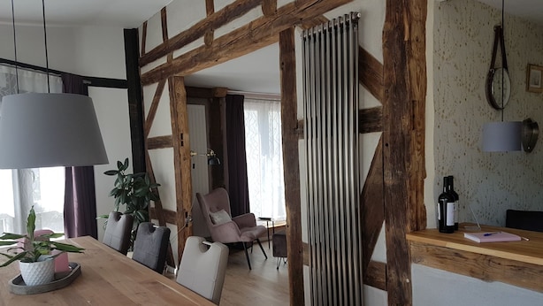 Ein modernes Wohnzimmer mit freiliegenden Holzbalken, einem Holzesstisch und einem großen Fenster.
