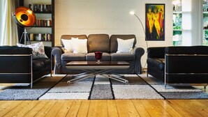 En moderne stue med sofaarrangement, sofabord, gulvlampe og bogreol.