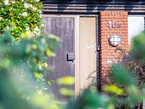 Une porte en bois avec une poignée en métal, un mur de briques avec une fenêtre et un petit luminaire extérieur.