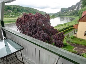 A balcony with a view of a river, greenery, and a building with a red roof. - Fewo Kuhstall by Interhome (Königstein)