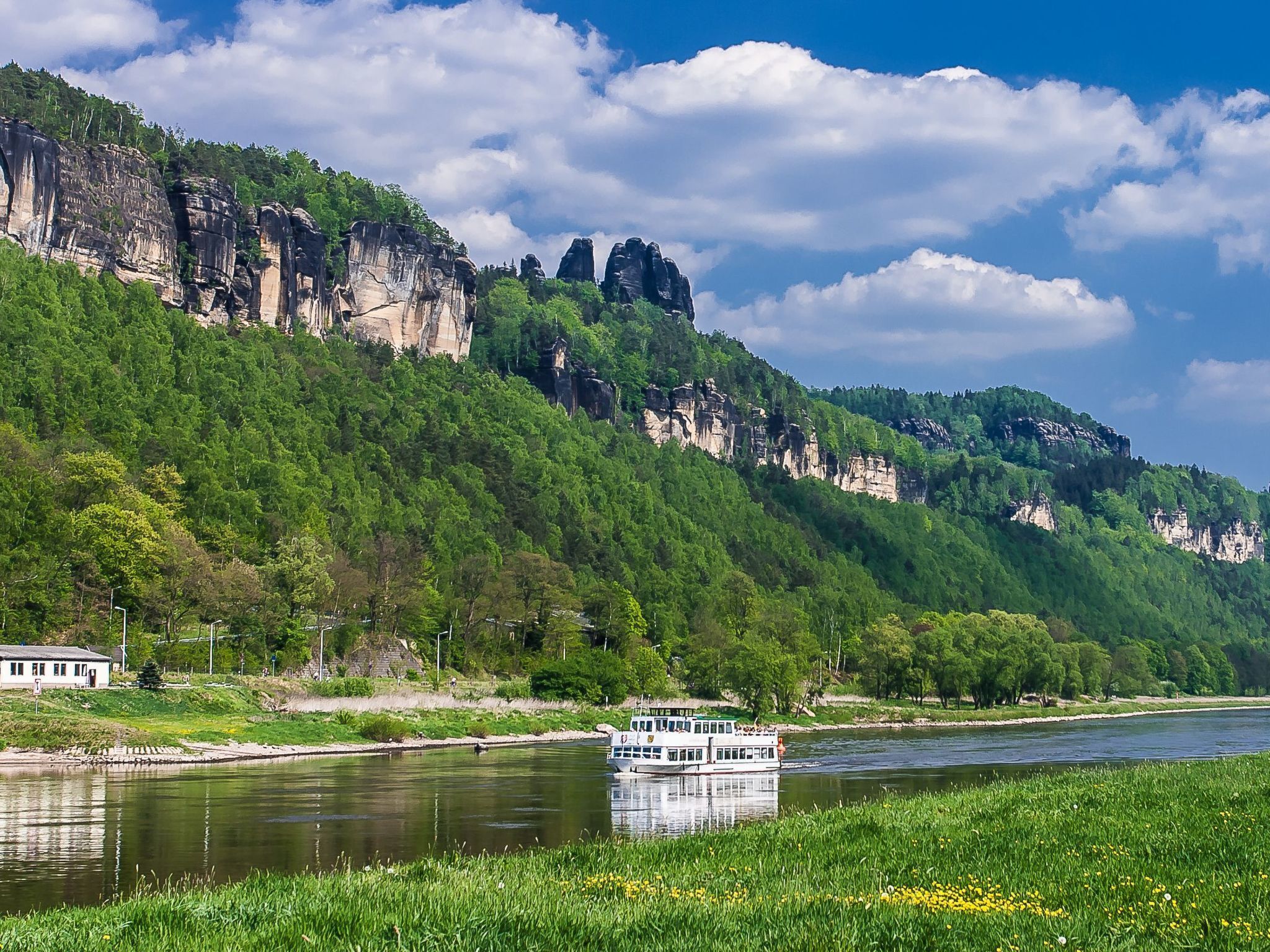 A river with a boat, surrounded by lush green hills and rocky cliffs.