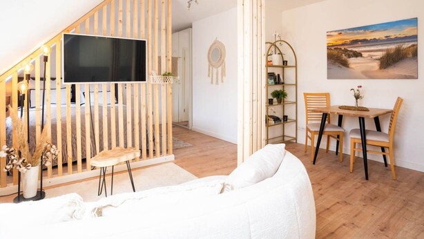 A modern loft with a wooden staircase, a flat-screen TV, a dining area with a table and chairs, and a large window with a beach view. - Schule Altes Land by Interhome (Jork)
