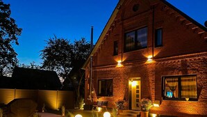 A brick house with a well-lit entrance, a visible number '83', and outdoor seating area with plants. - Schule Altes Land by Interhome (Jork)