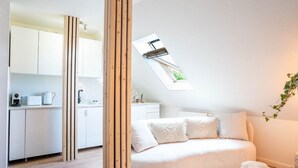A modern, well-lit room with a loft-style ceiling, a white sofa with patterned cushions, a small wooden table, and a skylight above the kitchen area. - Schule Altes Land by Interhome (Jork)