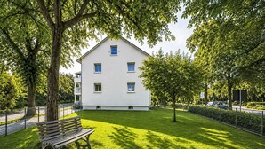 A white building with multiple windows, a grassy lawn, a bench, and trees. - Wohnung „Sonnendeck“ by Interhome (Laupheim)