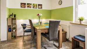 A dining area with a wooden table, chairs, a vase with flowers, and a shelf with a plant. - Wohnung „Sonnendeck“ by Interhome (Laupheim)