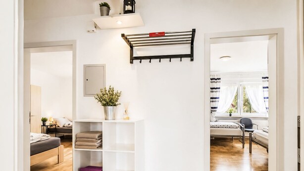 A modern interior with a white shelving unit, a hanging rack, and a view into a bedroom with a bed and a window. - Wohnung „Sonnendeck“ by Interhome (Laupheim)