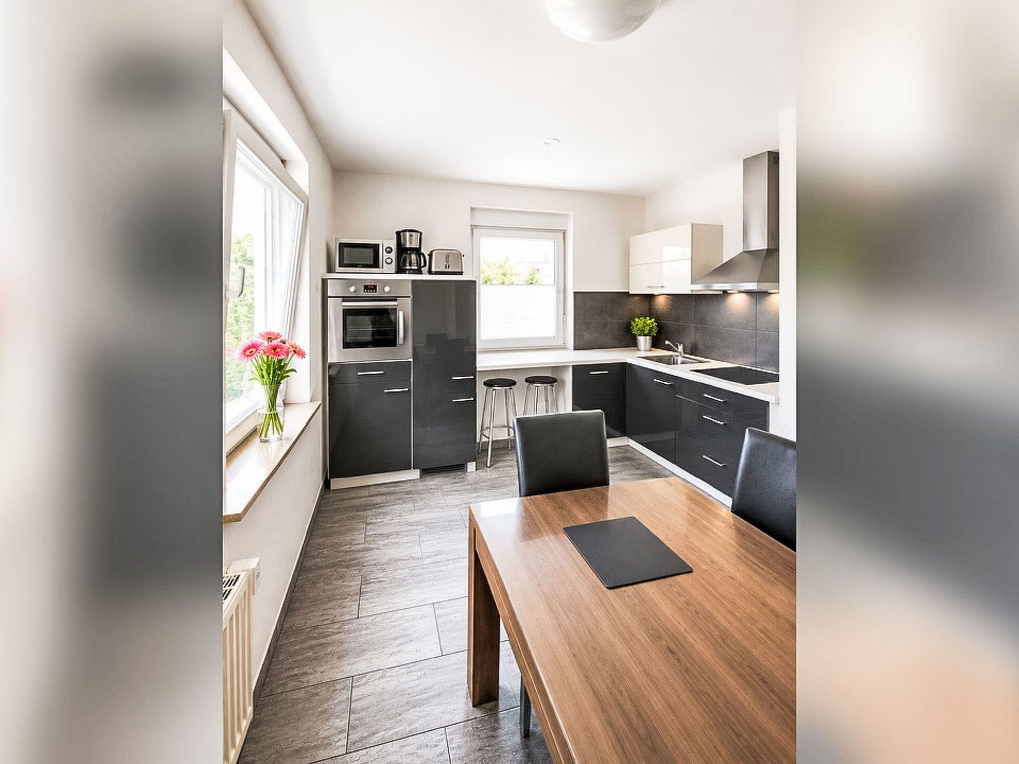 Une cuisine moderne avec un coin repas, comprenant une table et des chaises en bois, un four encastré et une fenêtre offrant une vue agréable.