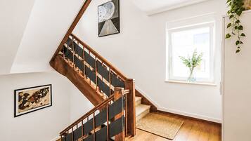Un escalier avec des rampes en bois et une main courante noire, menant à un palier où est accrochée une œuvre d’art encadrée, et une fenêtre donnant sur un paysage verdoyant.