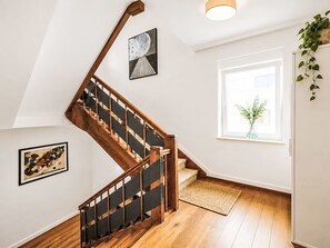 Eine Treppe mit Holzgeländern und einem schwarzen Handlauf, die zu einer Zwischenebene mit einem gerahmten Kunstwerk und einem Fenster mit Blick auf Grün führt.