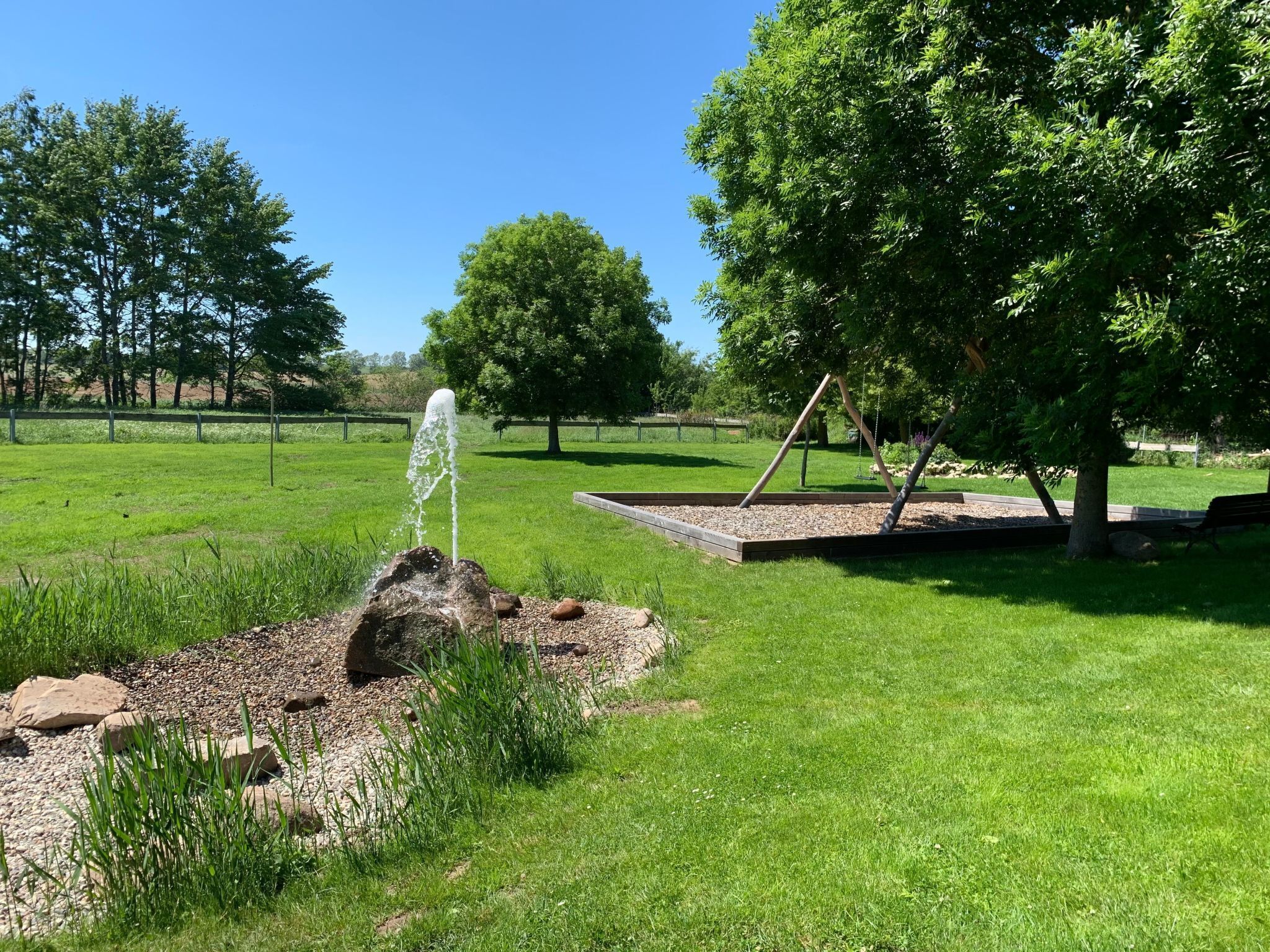 En grön park med en vattenfontän, en gunga och en bänk.