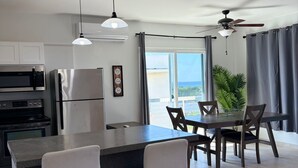 Una cucina moderna con isola centrale, sgabelli da bar, un tavolo da pranzo con sedie, un frigorifero, un forno a microonde e lampade a sospensione.