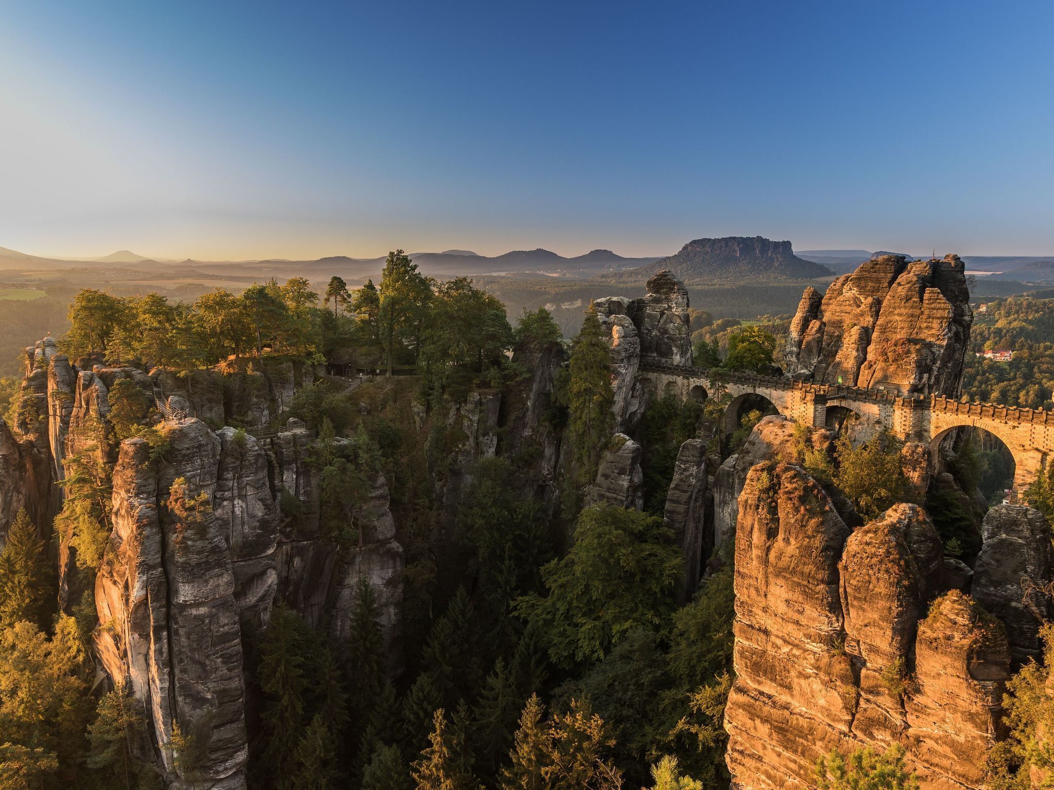 A panoramic view of a natural rock formation with a bridge connecting two cliffs.