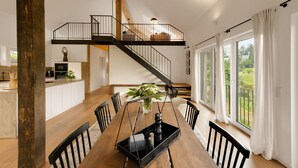 Een ruime eetruimte met een houten tafel, zwarte stoelen en een zwarte dienblad met een pepermolen. Een trap met een zwarte leuning leidt naar een hoger niveau.