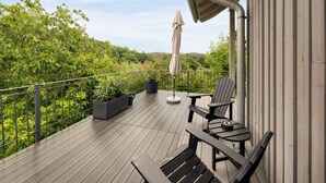 Een houten terras met buitenmeubilair, een bloempot en uitzicht op een bebost gebied.
