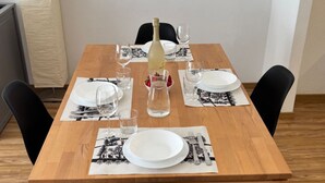 Une table à manger est dressée avec des assiettes, des couverts, des verres et une bouteille, et elle est entourée de chaises noires sur un plancher en bois.