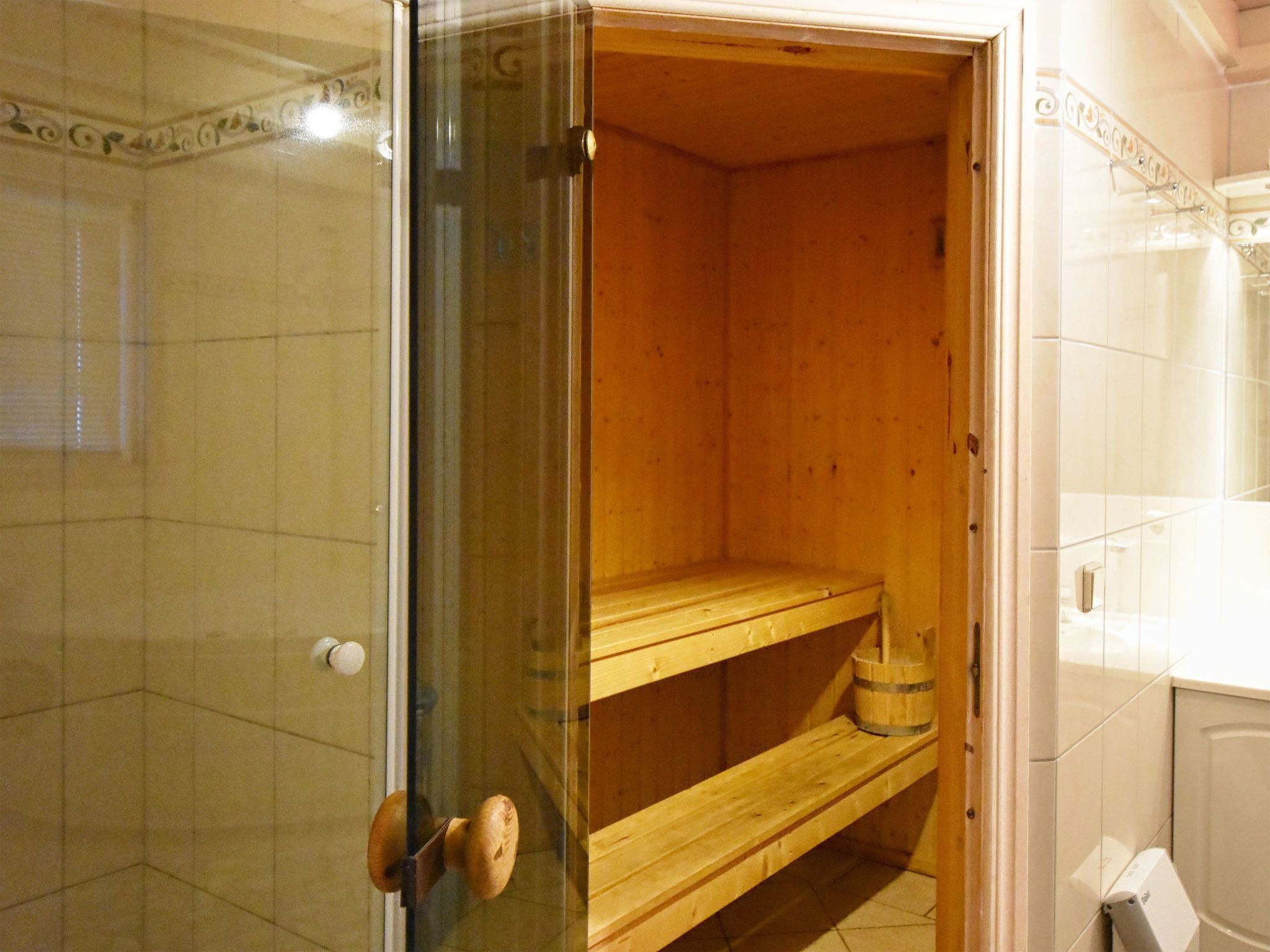 A wooden sauna with a glass door, a wooden bench, and a bucket.