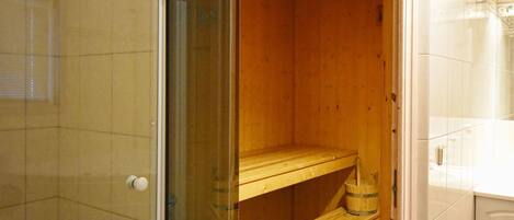 A wooden sauna with a glass door, a wooden bench, and a bucket.