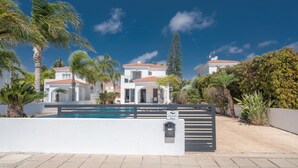 Una villa moderna con piscina, circondata da palme e un cielo azzurro intenso.