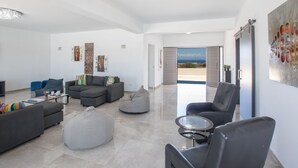 A spacious living room with a modern chandelier, a gray sofa set, a glass coffee table, and a view through an open door to the outside. - Geräumiges Ferienhaus für 12 Personen in Paralini by Interhome (Paralimni)