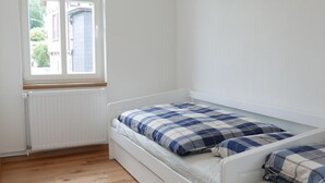 A room with a single bed, a window, and wooden flooring.