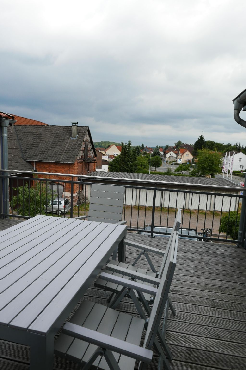 Une terrasse en bois avec une table et des chaises, donnant sur un quartier résidentiel avec des maisons et une route.