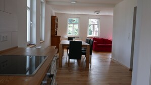 A modern kitchen with a wooden countertop and built-in appliances, a dining area with a wooden table and chairs, and a red sofa in a bright room with large windows.