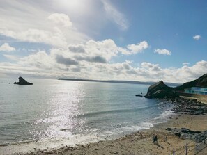 Una spiaggia costiera con un promontorio roccioso, mare calmo e cielo sereno.