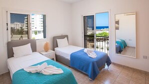 Een hotelkamer met twee bedden, een balkon met uitzicht op zee en een grote spiegel aan de wand.