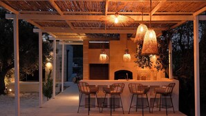 An outdoor bar area with a stone fireplace, hanging wicker lamps, and three bar stools. - Design-led masseria with infinity pool: vineyards, olives, beaches & Puglia (Manduria)
