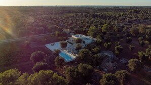 An aerial view of a modern villa with a pool, surrounded by dense vegetation and a clear sky. - Design-led masseria with infinity pool: vineyards, olives, beaches & Puglia (Manduria)