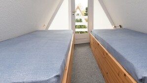 A small, narrow room with two single beds, a door leading outside, and a sloped ceiling. - Carolin by Interhome (Baabe)