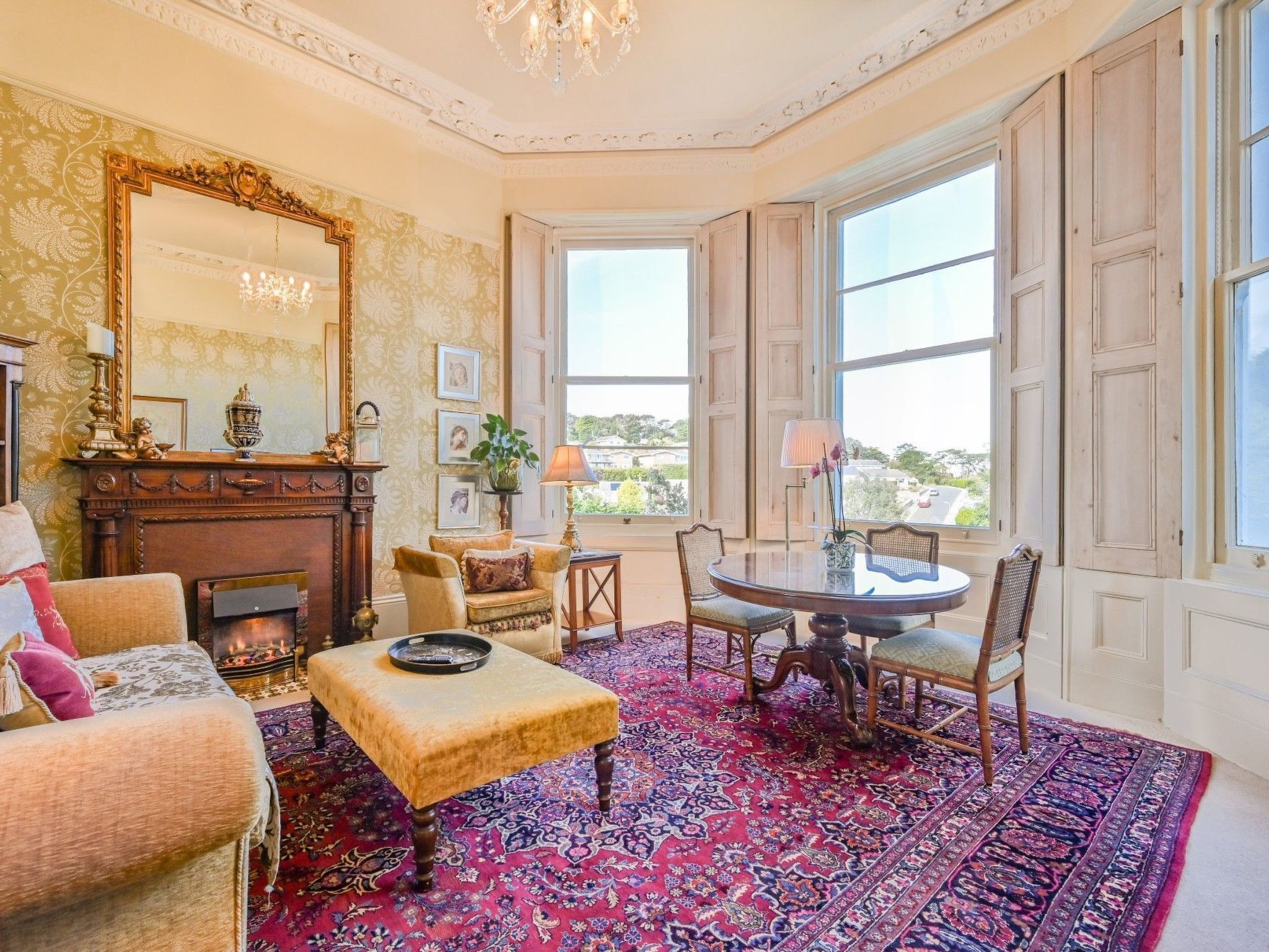 A room with a fireplace, a large mirror, a dining table with chairs, and a patterned rug.