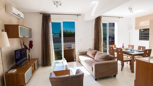 Ein modernes Wohnzimmer mit Sofa, Couchtisch, Fernseher und Essbereich mit Stühlen und Tisch.