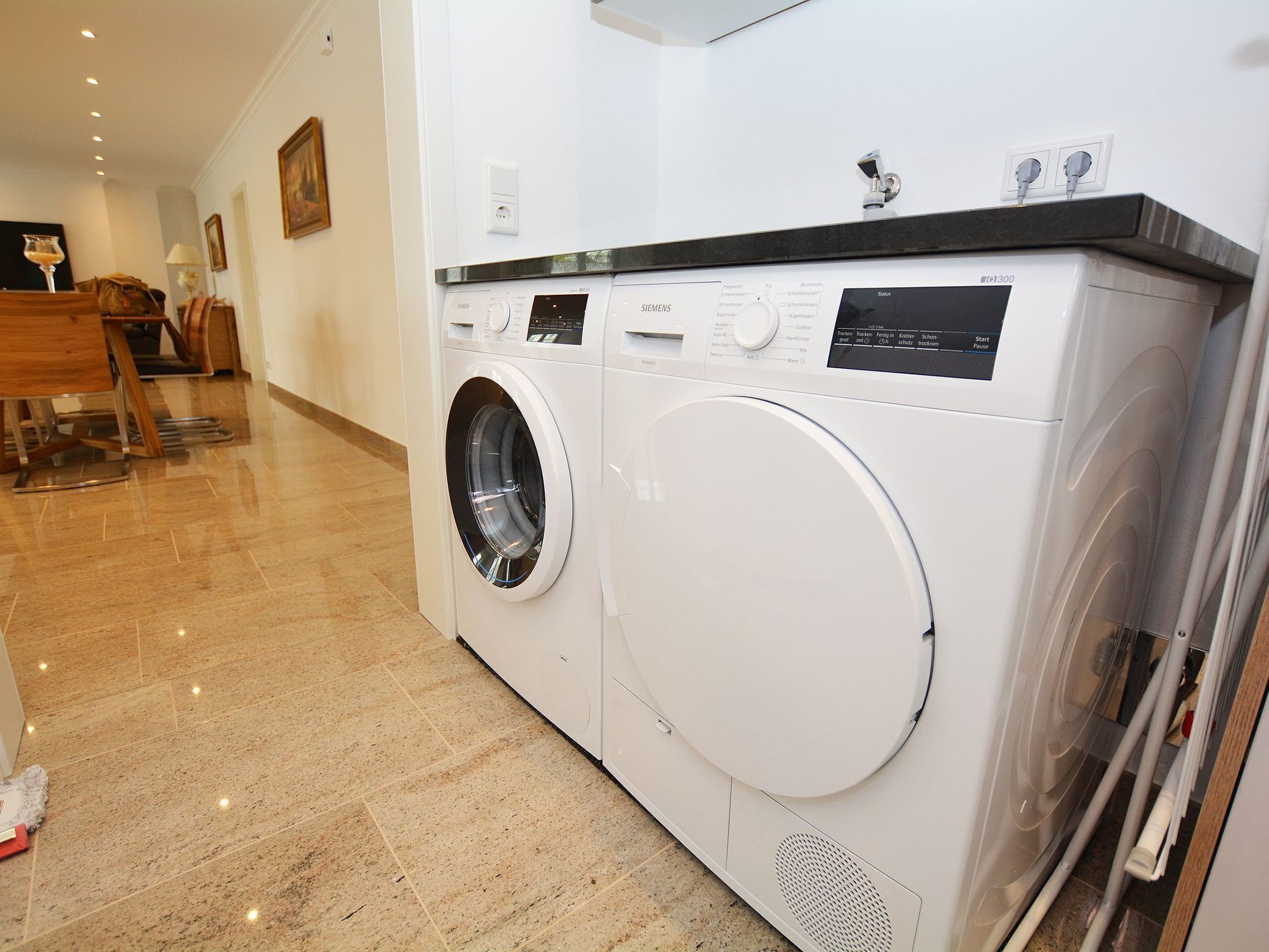 A front-loading washing machine in a well-lit room with a tiled floor.