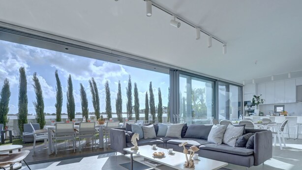 Un salón amplio con un gran ventanal que ofrece vistas panorámicas, una cocina moderna y un comedor con mobiliario de exterior.