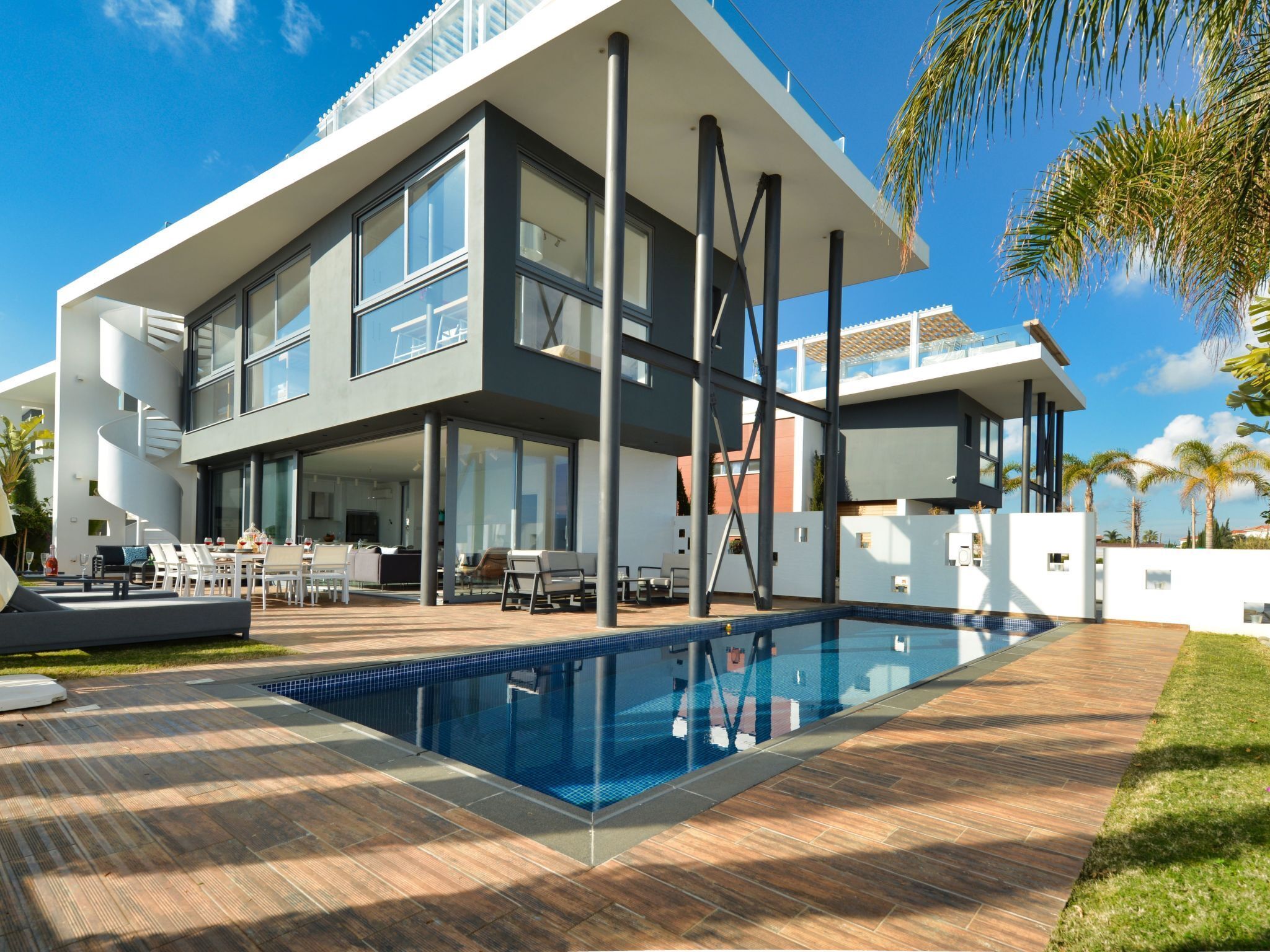 A modern two-story house with a swimming pool, outdoor seating, and a clear blue sky.