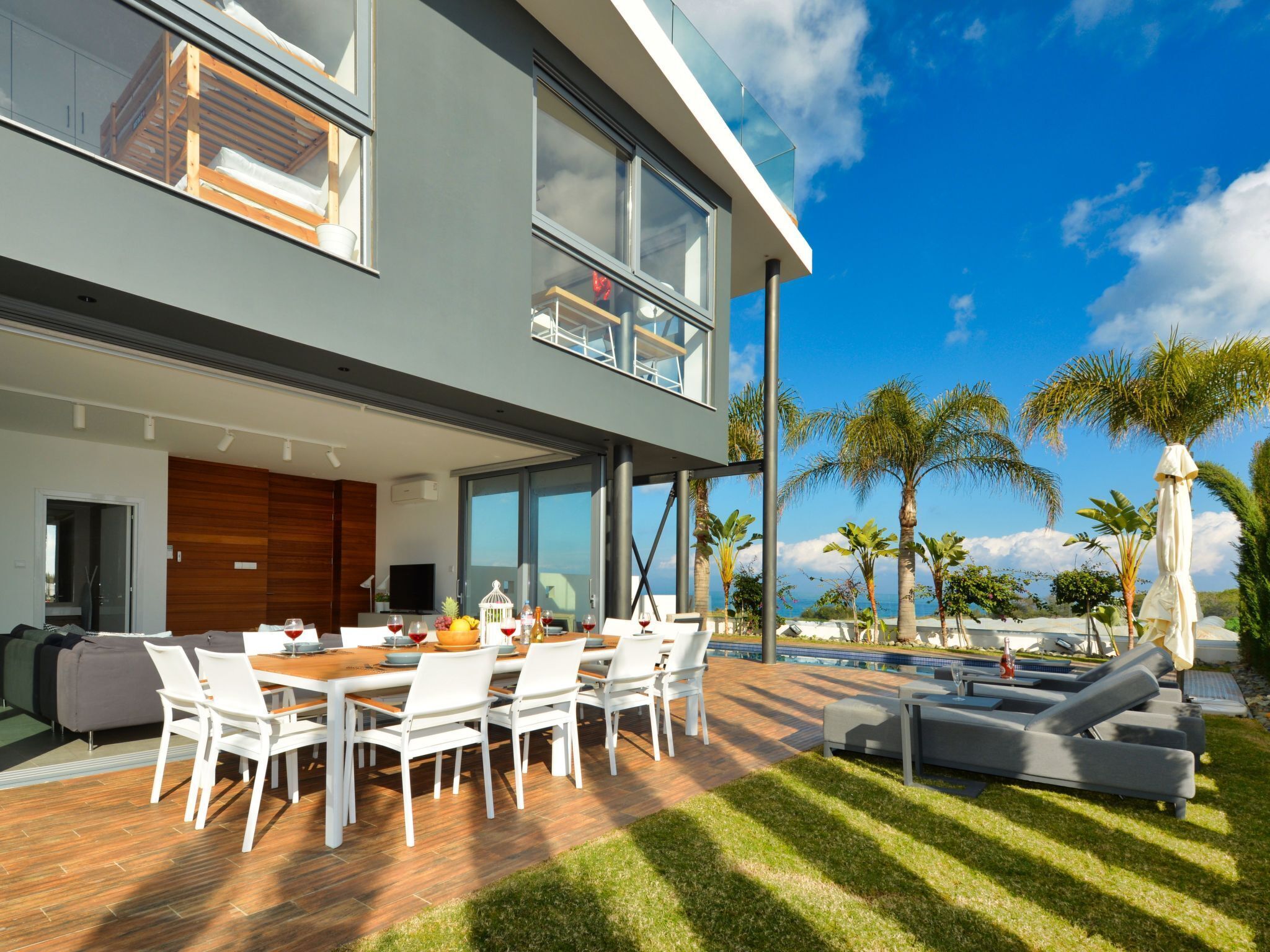 A modern two-story house with a dining area, outdoor pool, and tropical plants.