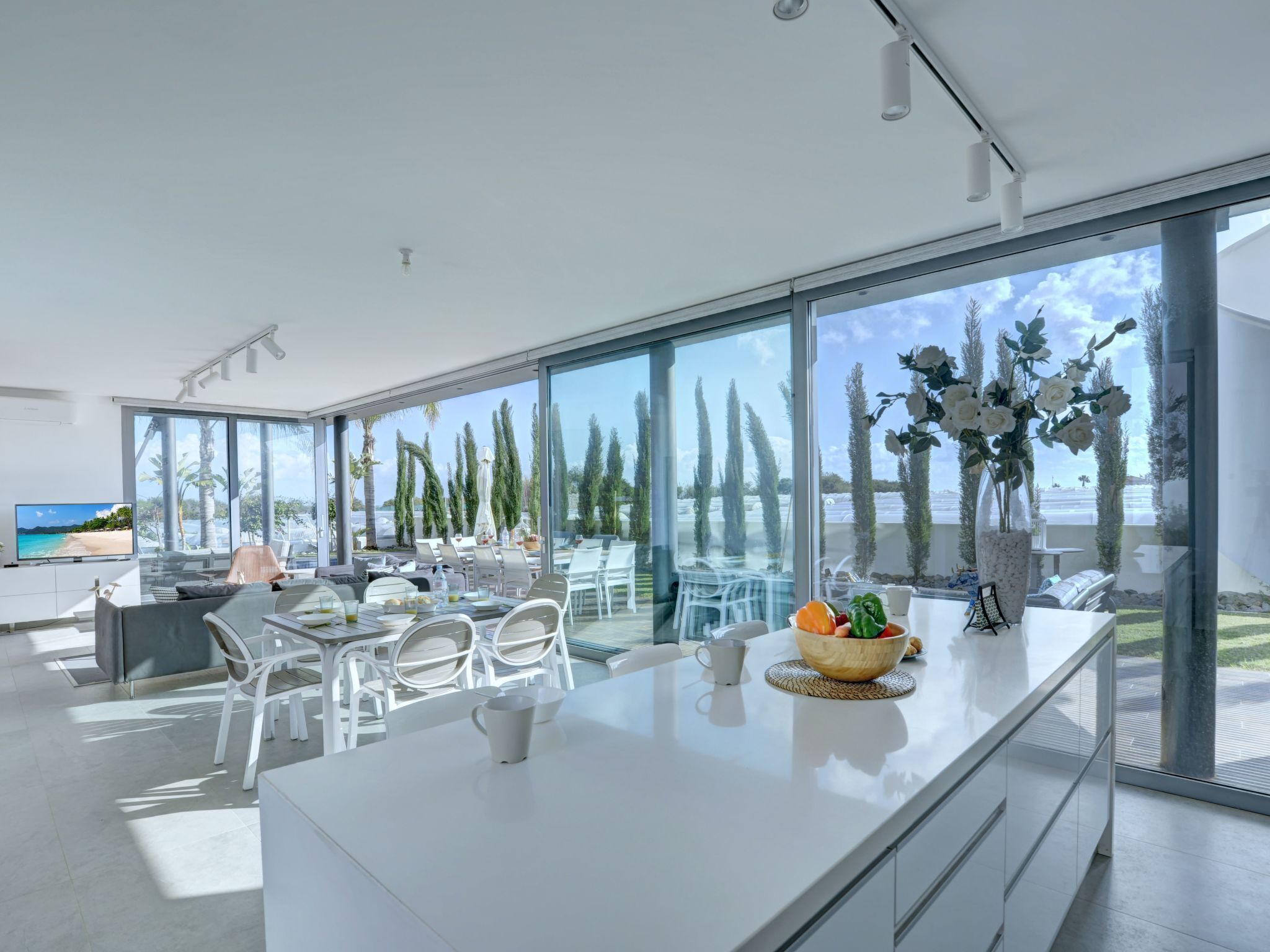 A modern kitchen with a large island, white cabinetry, and a view of the beach.