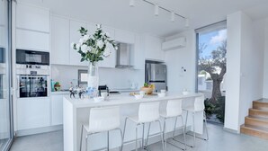 Una cocina moderna con armarios blancos, una isla central con taburetes y un amplio ventanal con vistas a un jardín.