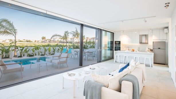 A modern living room with a large glass door leading to a pool area, a kitchen with white cabinets, and a view of the countryside. - Neue, moderne 3-Schlafzimmer-Villa mit privatem Pool by Interhome (Paralimni)