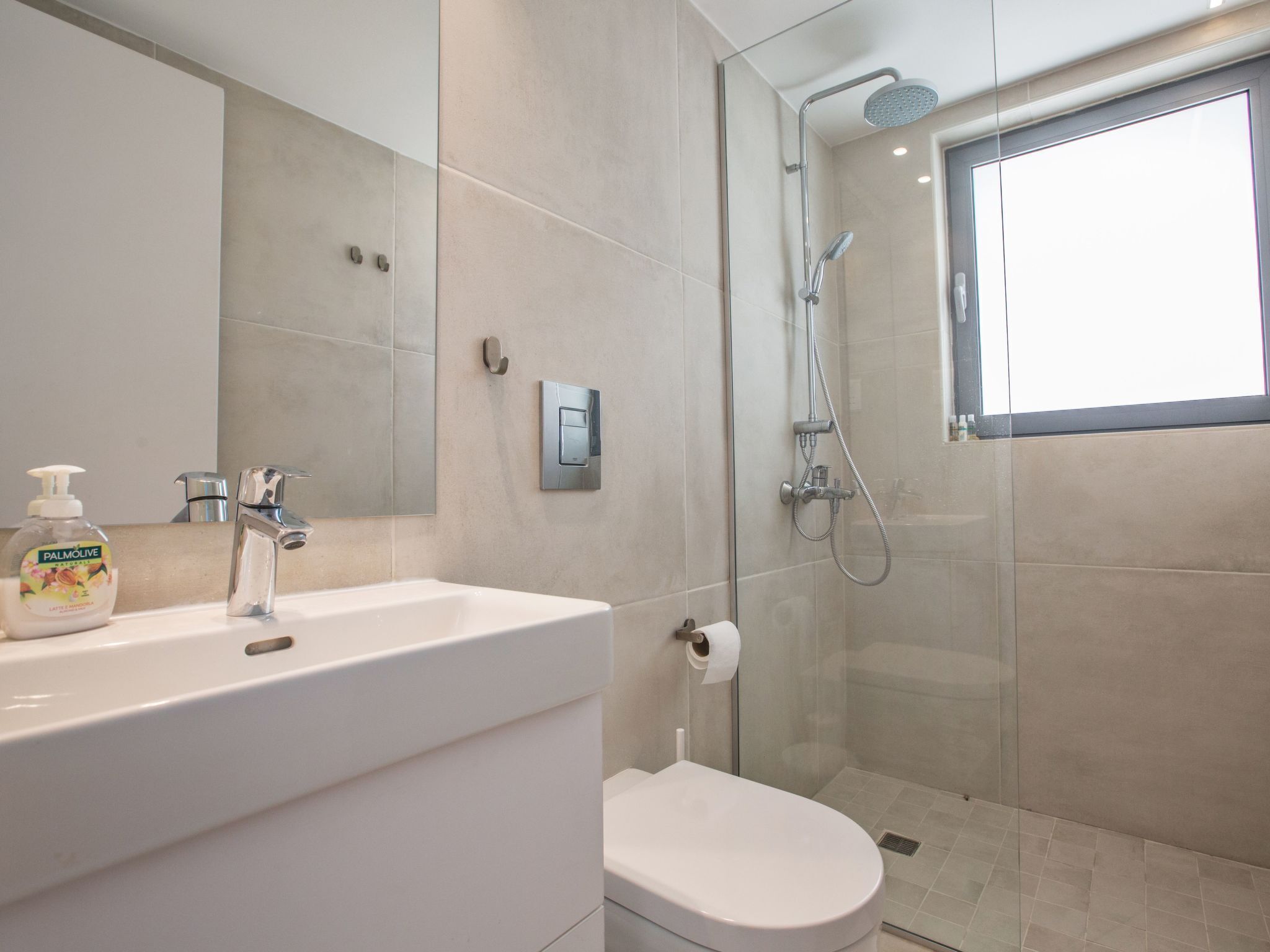 Un baño moderno con lavamanos blanco, inodoro y zona de ducha con mampara de vidrio.