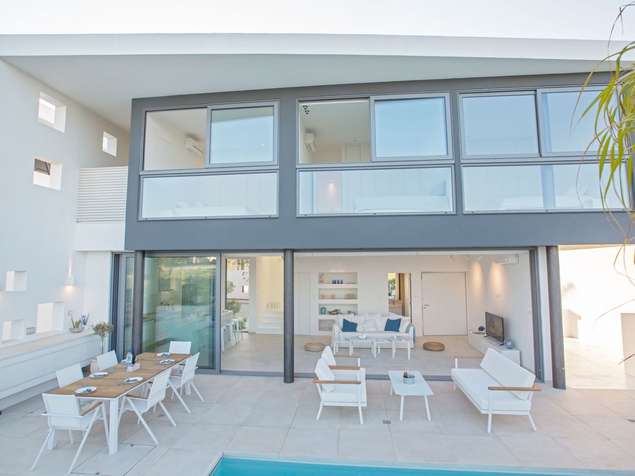 A modern two-story house with a pool, outdoor seating, and a well-lit interior.