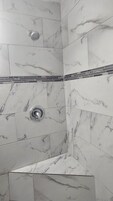 Zona de ducha con azulejos de mármol blanco y un borde de mosaico blanco y negro.