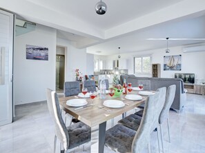 Ein moderner Essbereich mit einem Holztisch, gedeckten Plätzen für sechs Personen, grau gepolsterten Stühlen und einer Küche im Hintergrund.